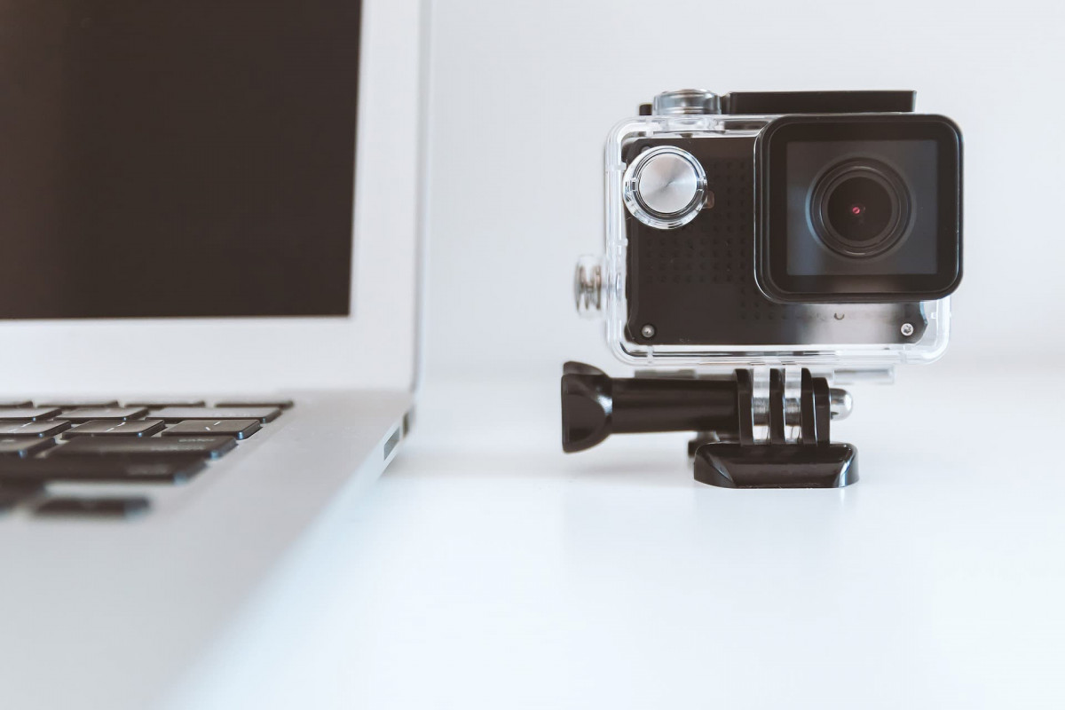 A GoPro stye camera stood next to a laptop