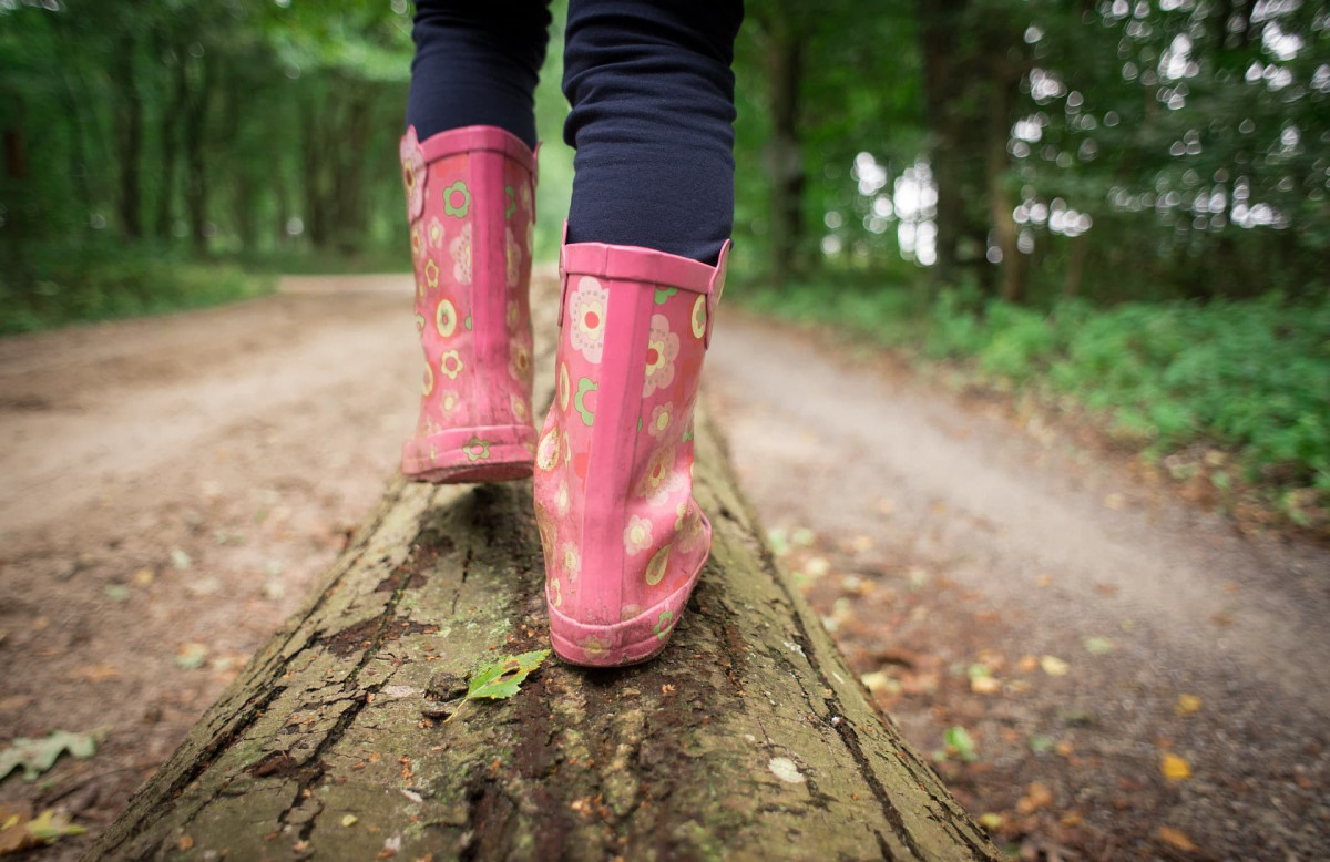 Child walking through a forest wearing wellies